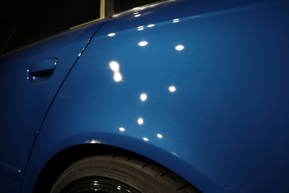 A close up of a blue car 's fender with white spots on it