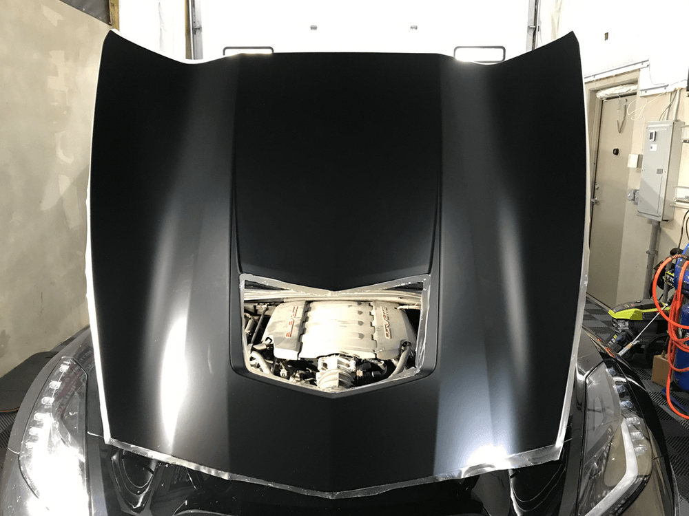 The hood of a black sports car is open and the engine is visible.