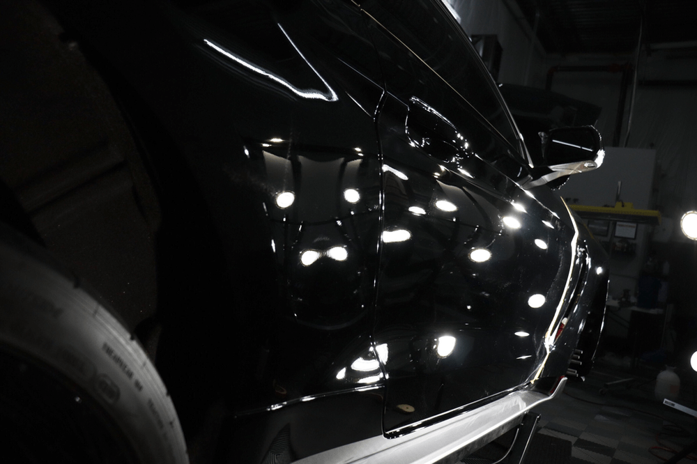 A black car is parked in a dark room in a garage.