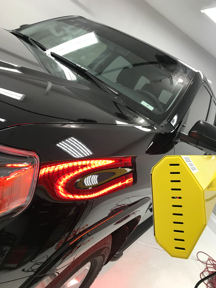 A black car is sitting next to a yellow object in a garage.