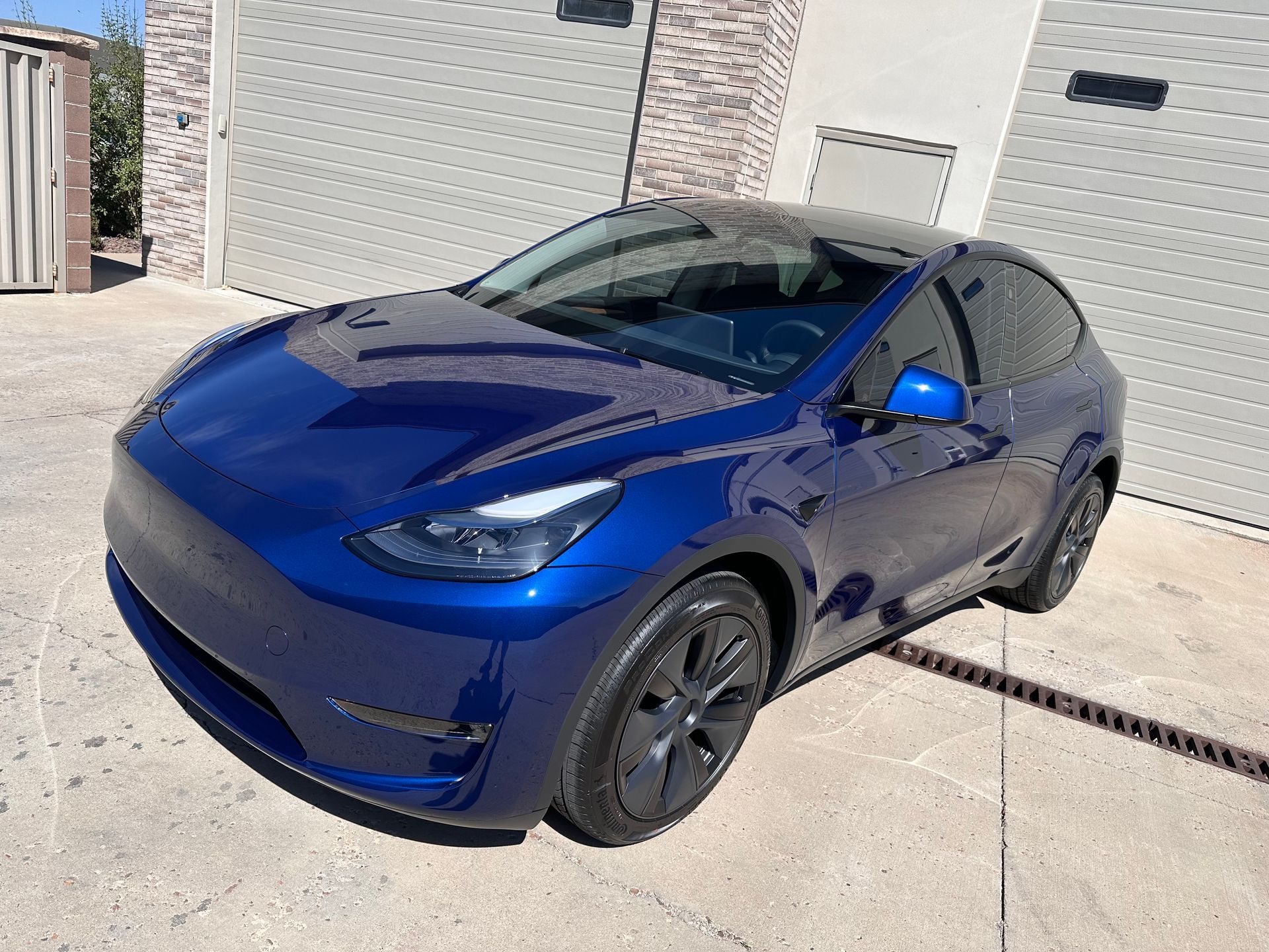 A blue tesla model y is parked in front of a garage.