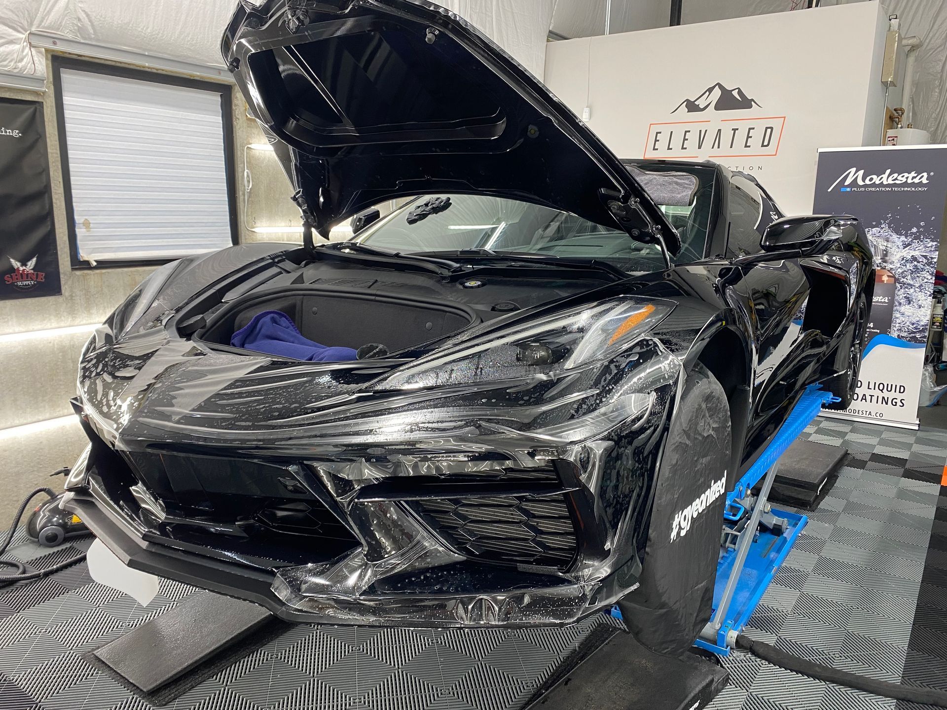 A black sports car with the hood open is sitting on a lift in a garage.