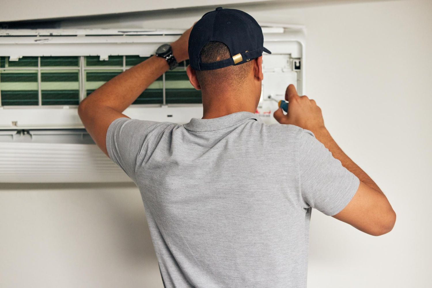 A man is fixing an air conditioner with a screwdriver.