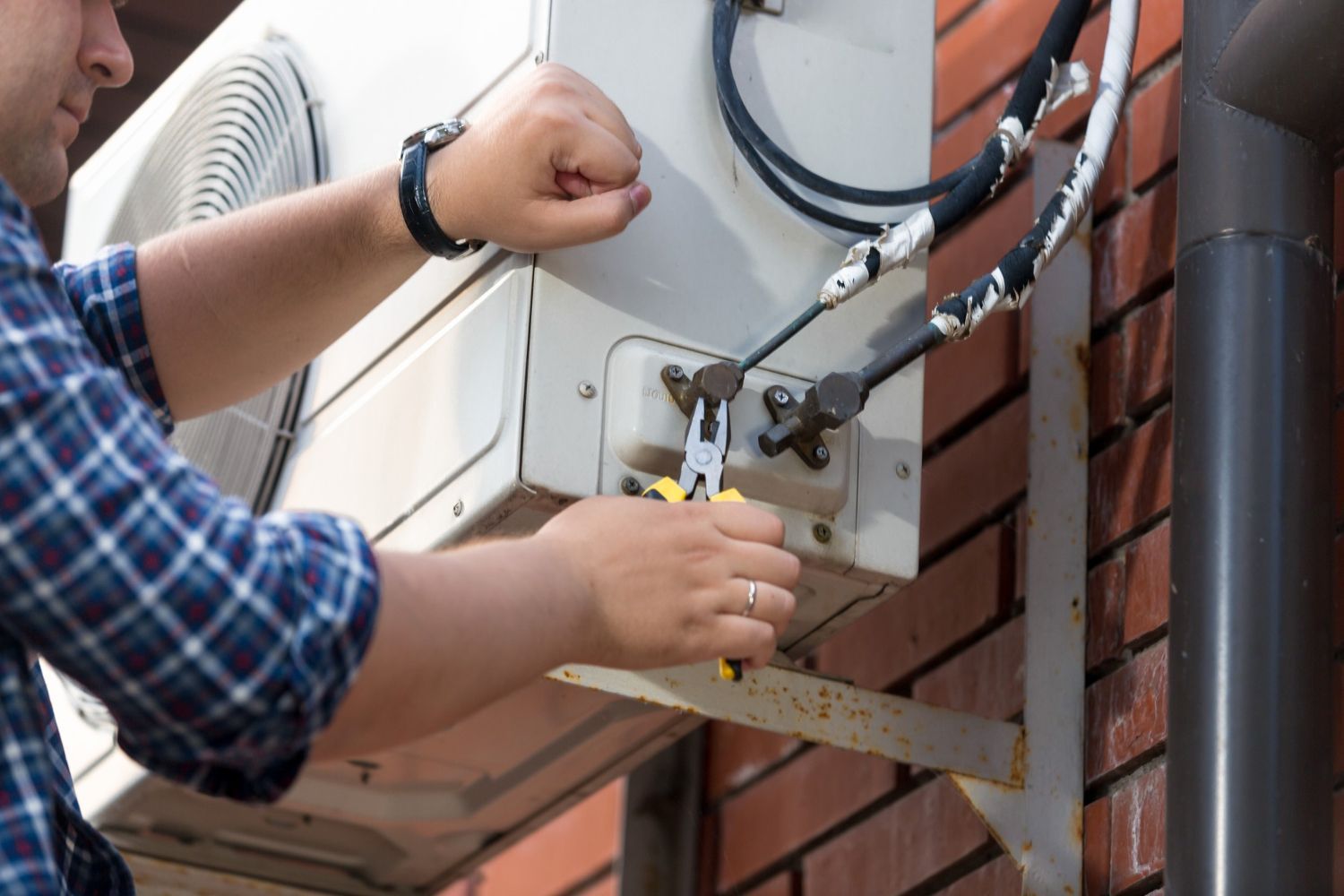 A man is fixing an air conditioner on the side of a building.