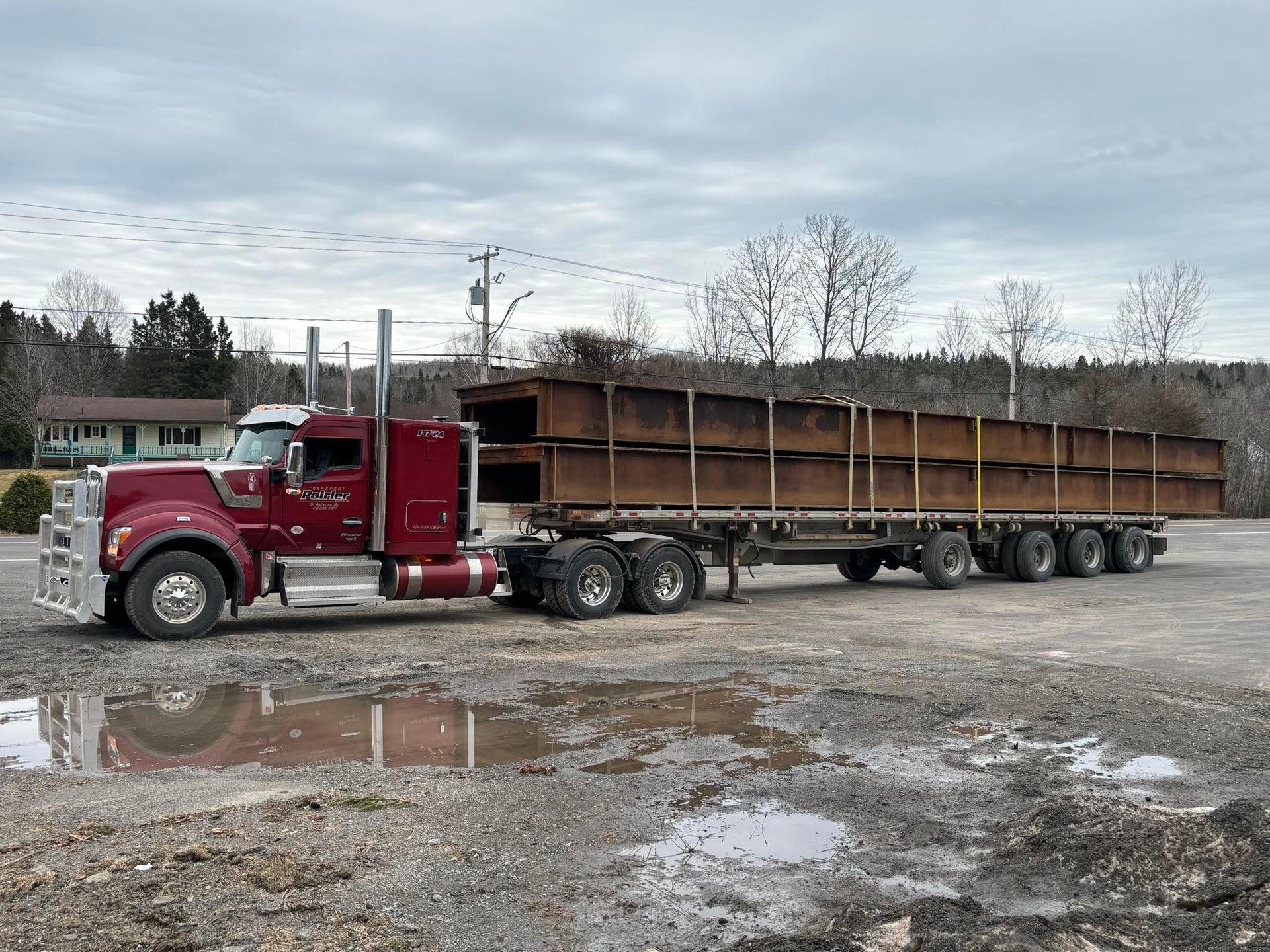 Un semi-remorque rouge avec une remorque à plateau transporte un gros morceau de métal.