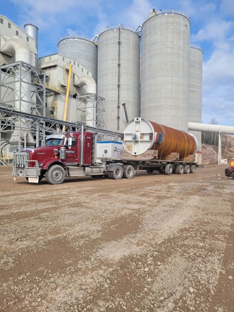 Un semi-camion rouge transporte un grand réservoir devant une usine.