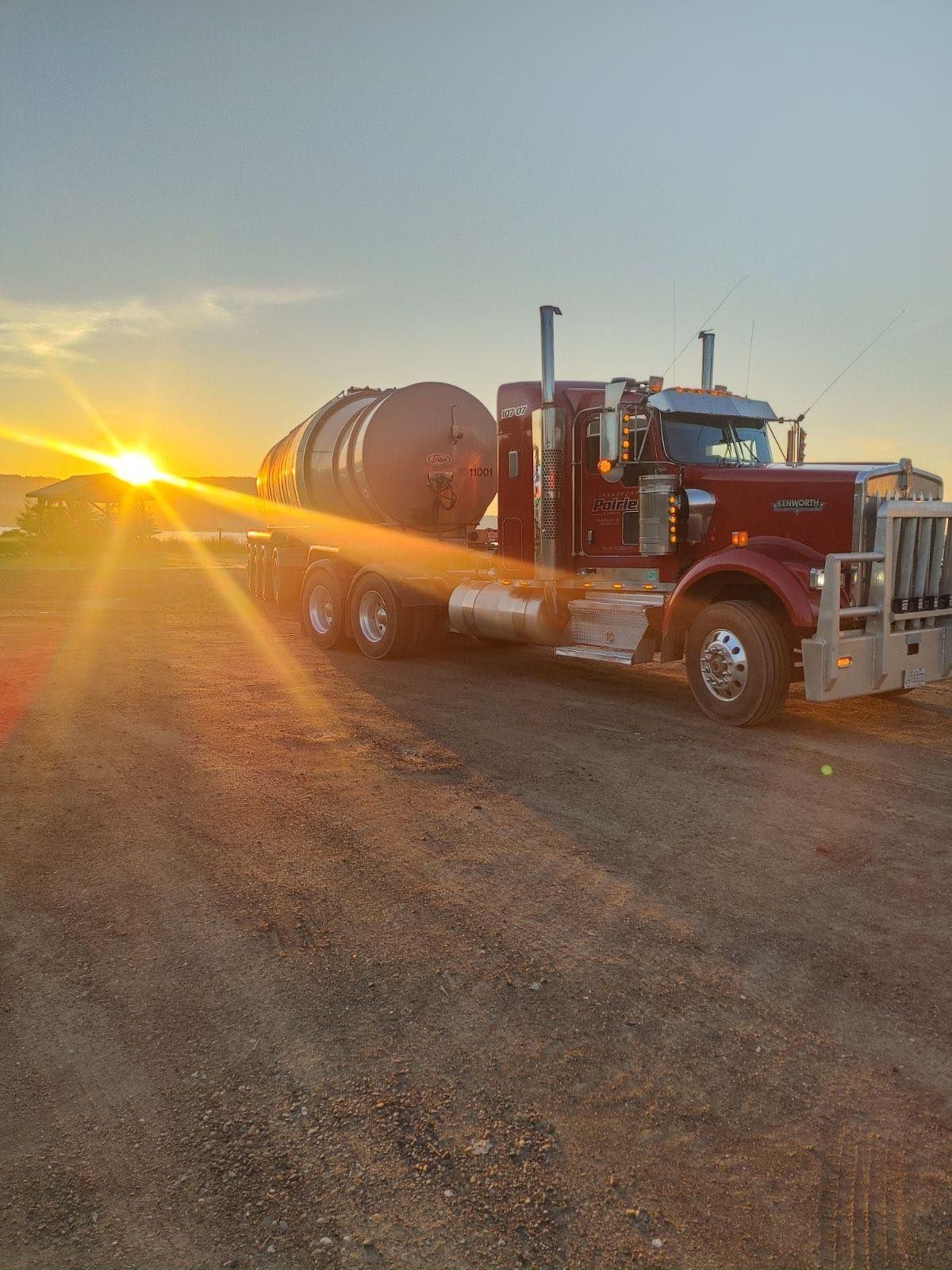 Un semi-camion rouge est garé sur le bord de la route au coucher du soleil.