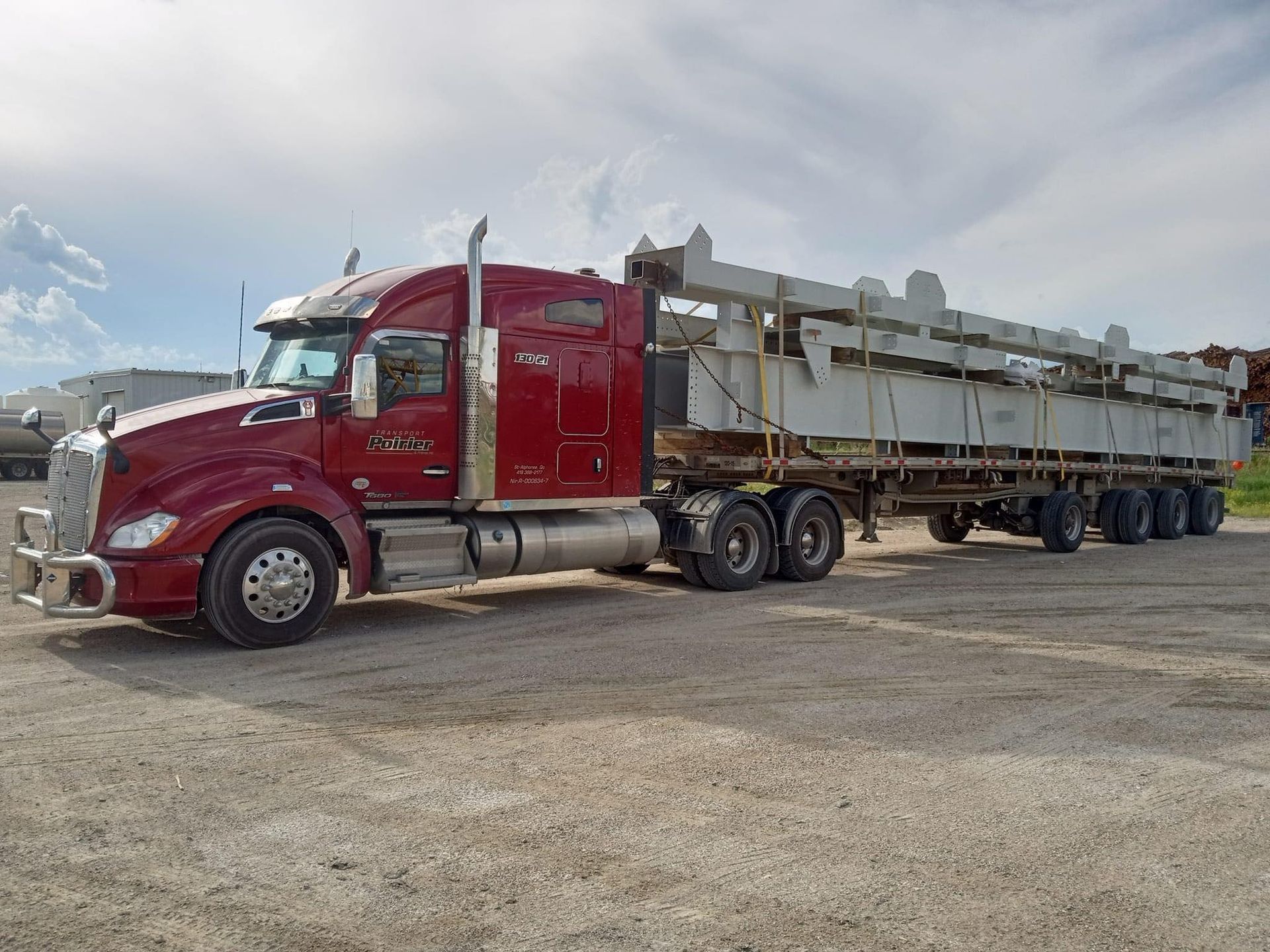Un semi-remorque rouge est garé sur un terrain en gravier.