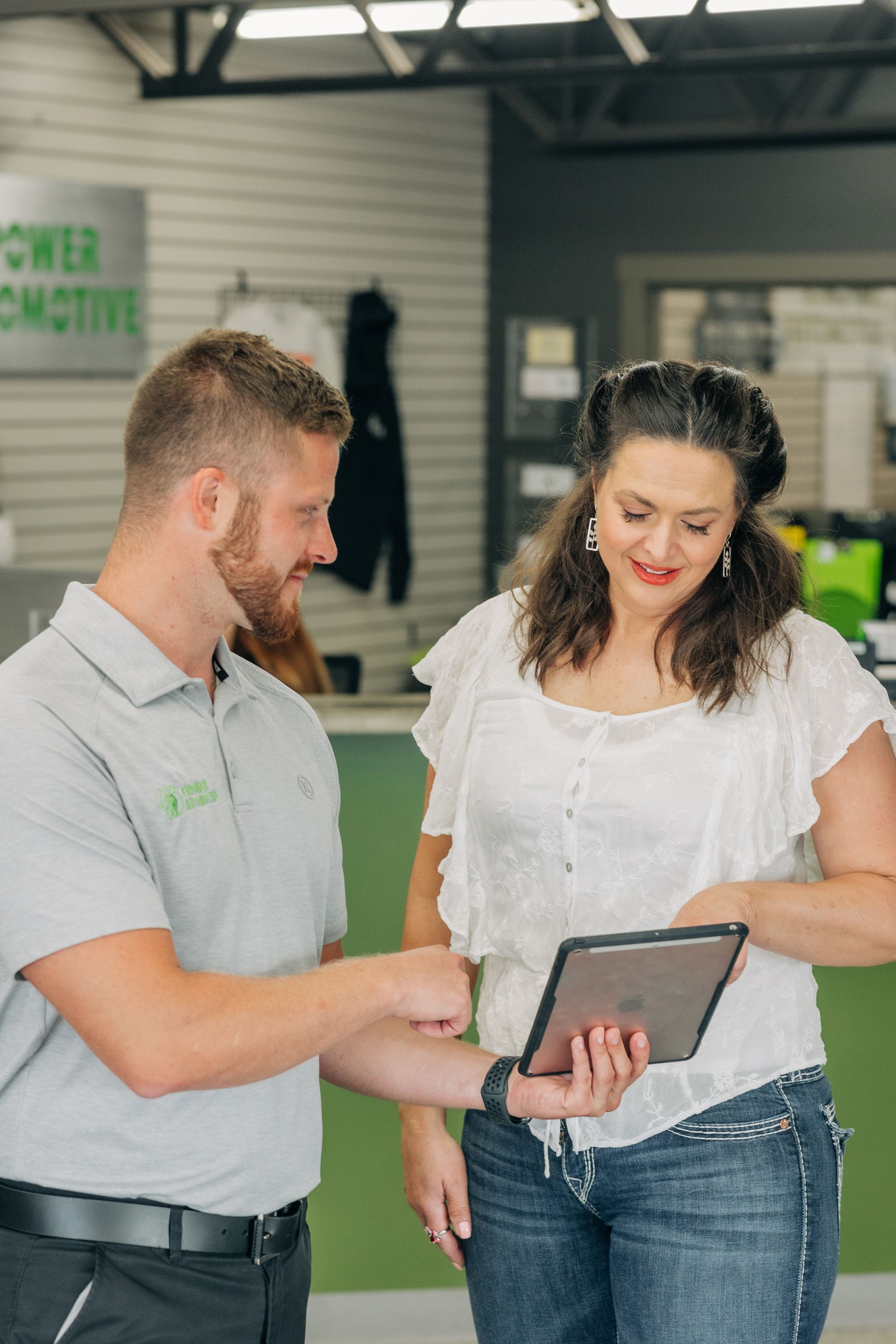 Man in gray shirt shows woman on tablet; automotive shop setting. | Empower Automotive