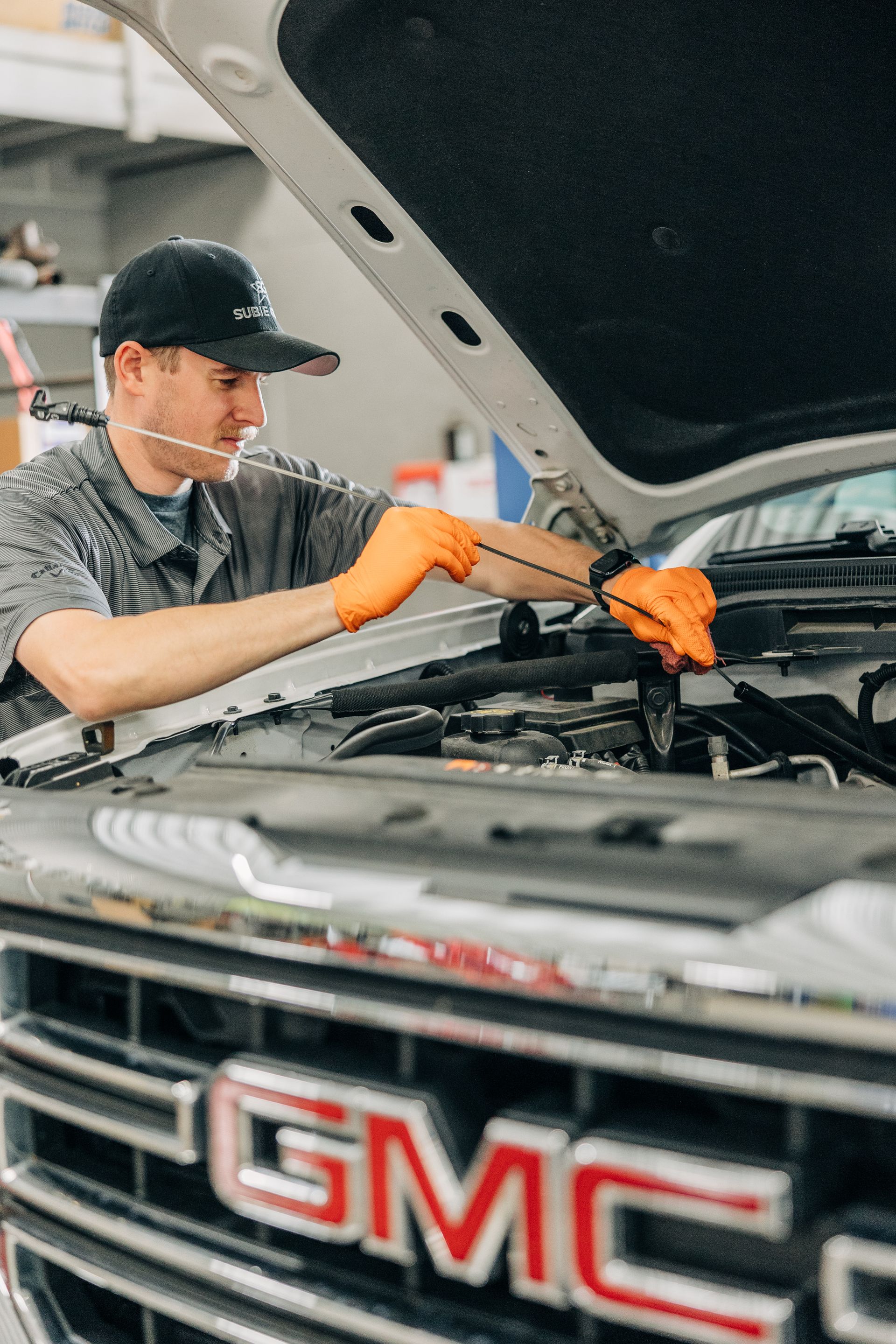 Mechanic in orange gloves working on a GMC truck engine, under the hood.