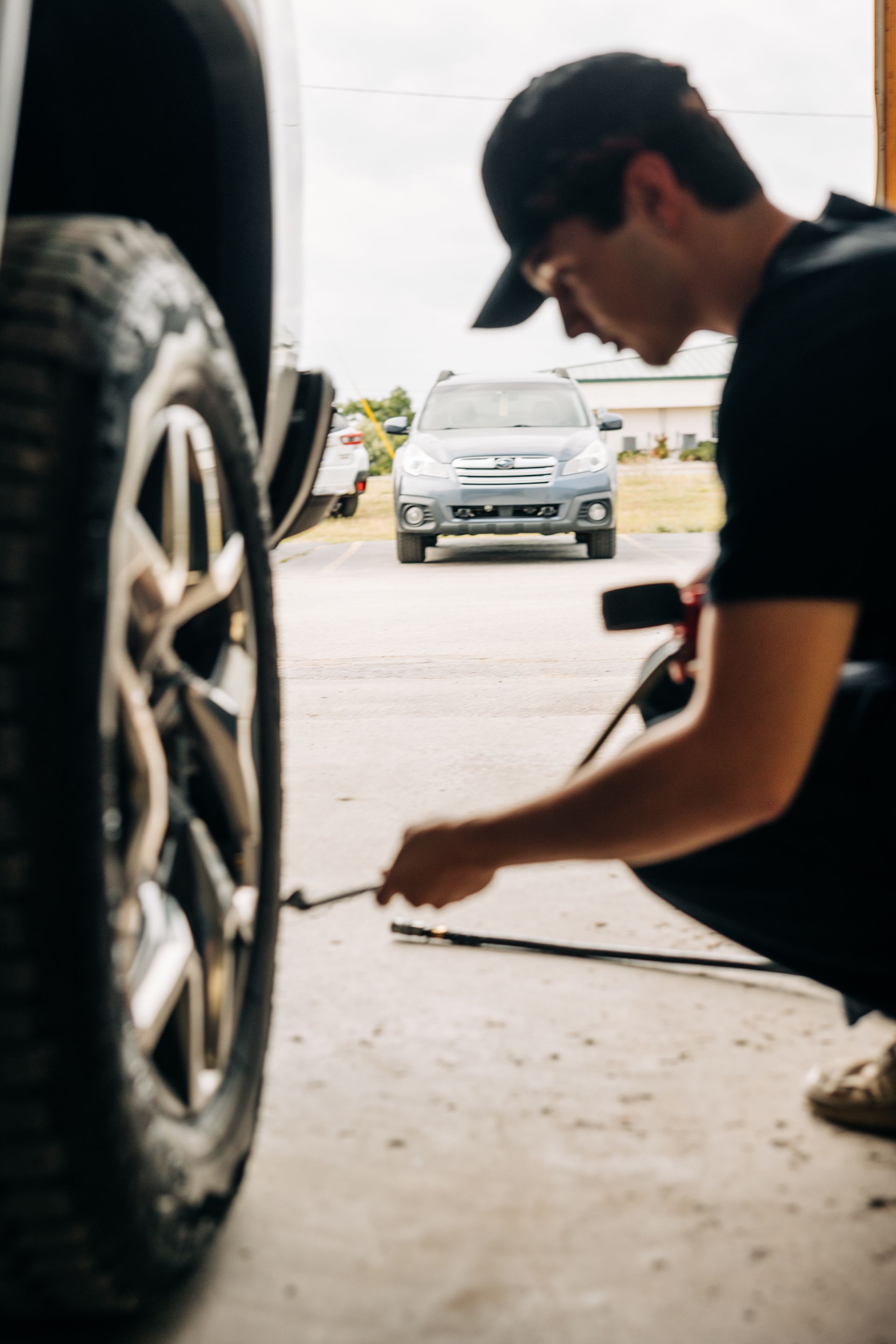 A man inflates a tire with a wrench near a gray car in a garage.