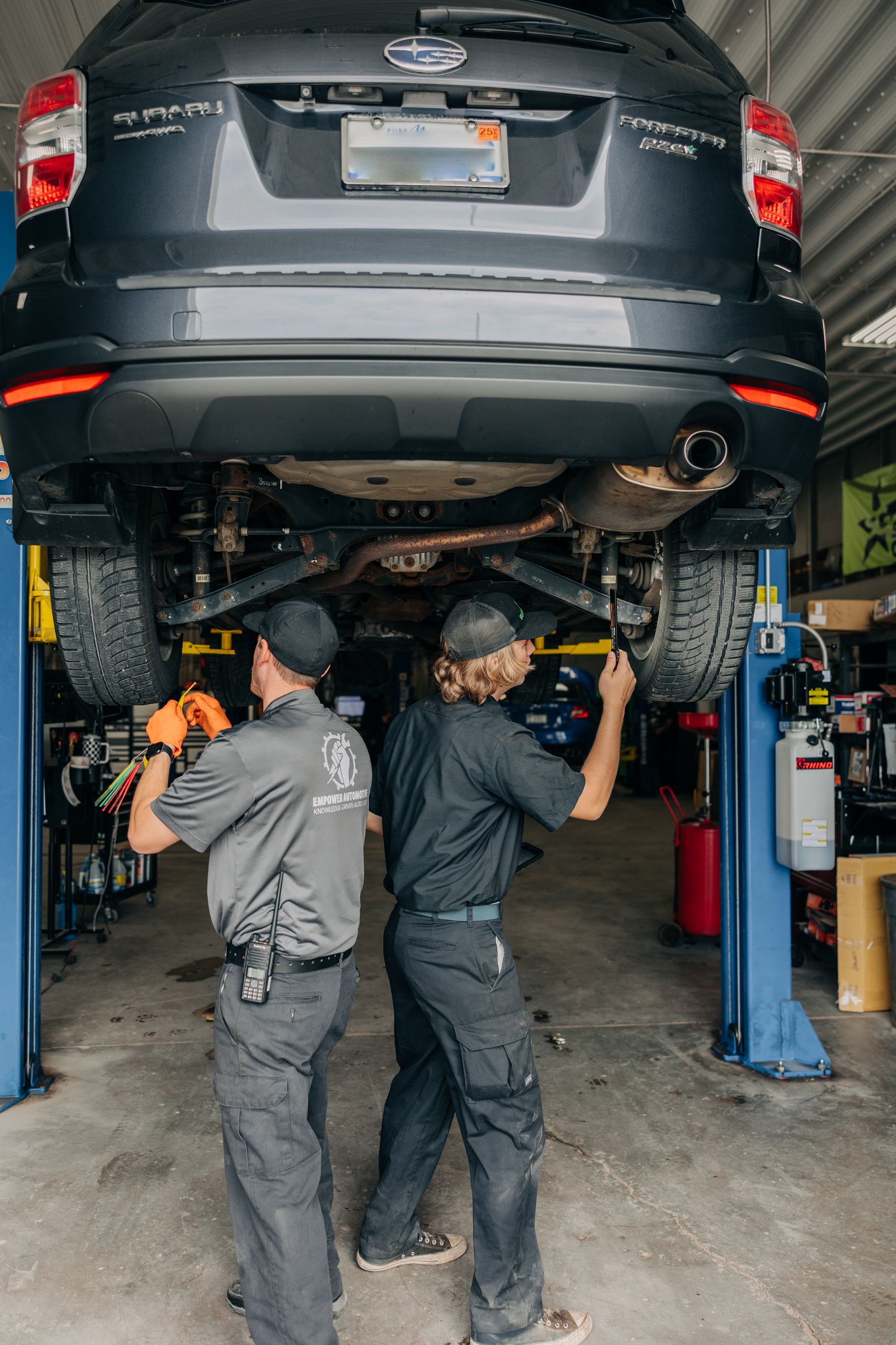 Two mechanics working on a gray SUV raised on a lift in a garage. | Empower Automotive