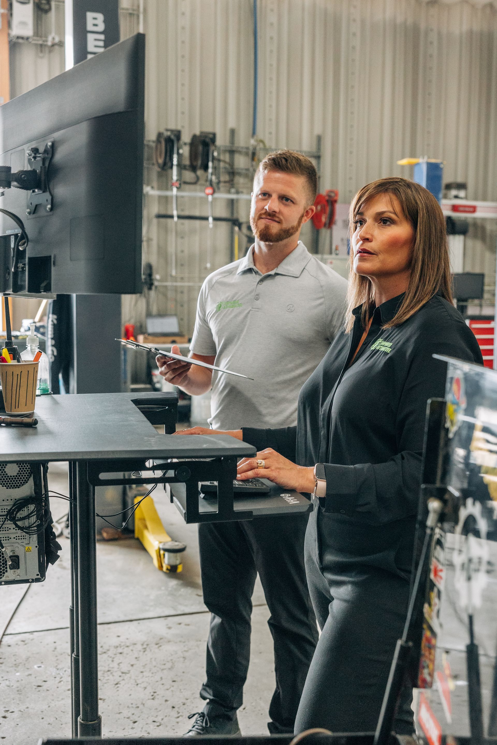 Two people in an auto shop looking at a large screen. Man holds a tablet, woman gestures. | Empower Automotive