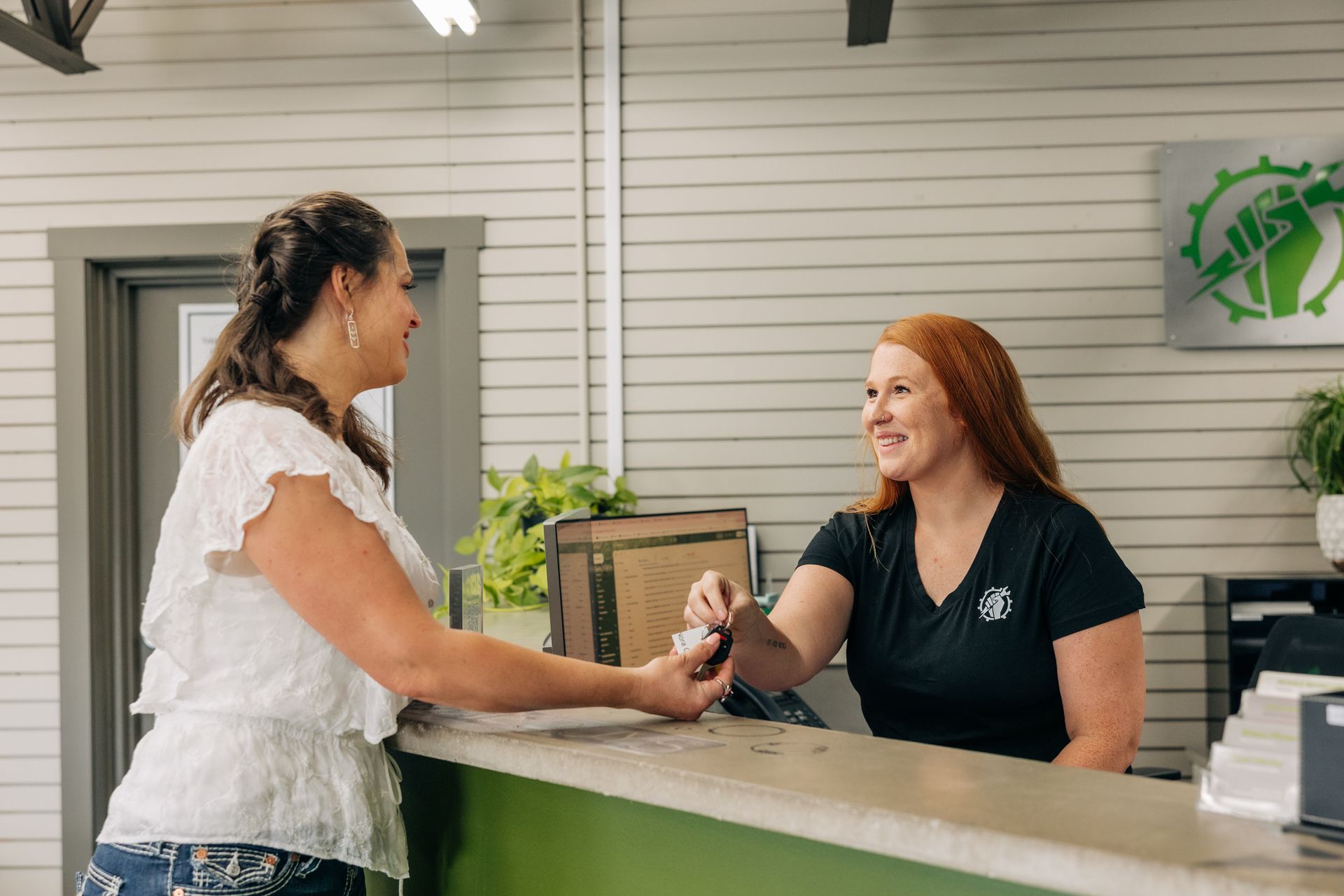 Woman receiving keys from a smiling receptionist at a green-accented desk in a business setting. | Empower Automotive