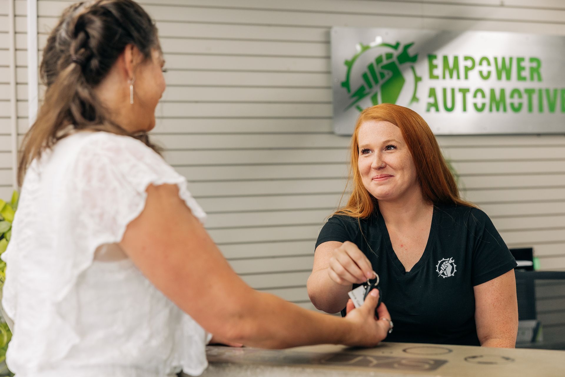 Woman handing keys to another woman at Empower Automotive counter. | Empower Automotive