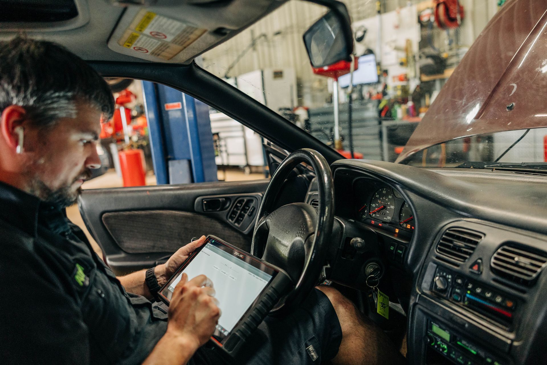 Mechanic using a tablet to diagnose a car's engine in a garage. | Empower Automotive
