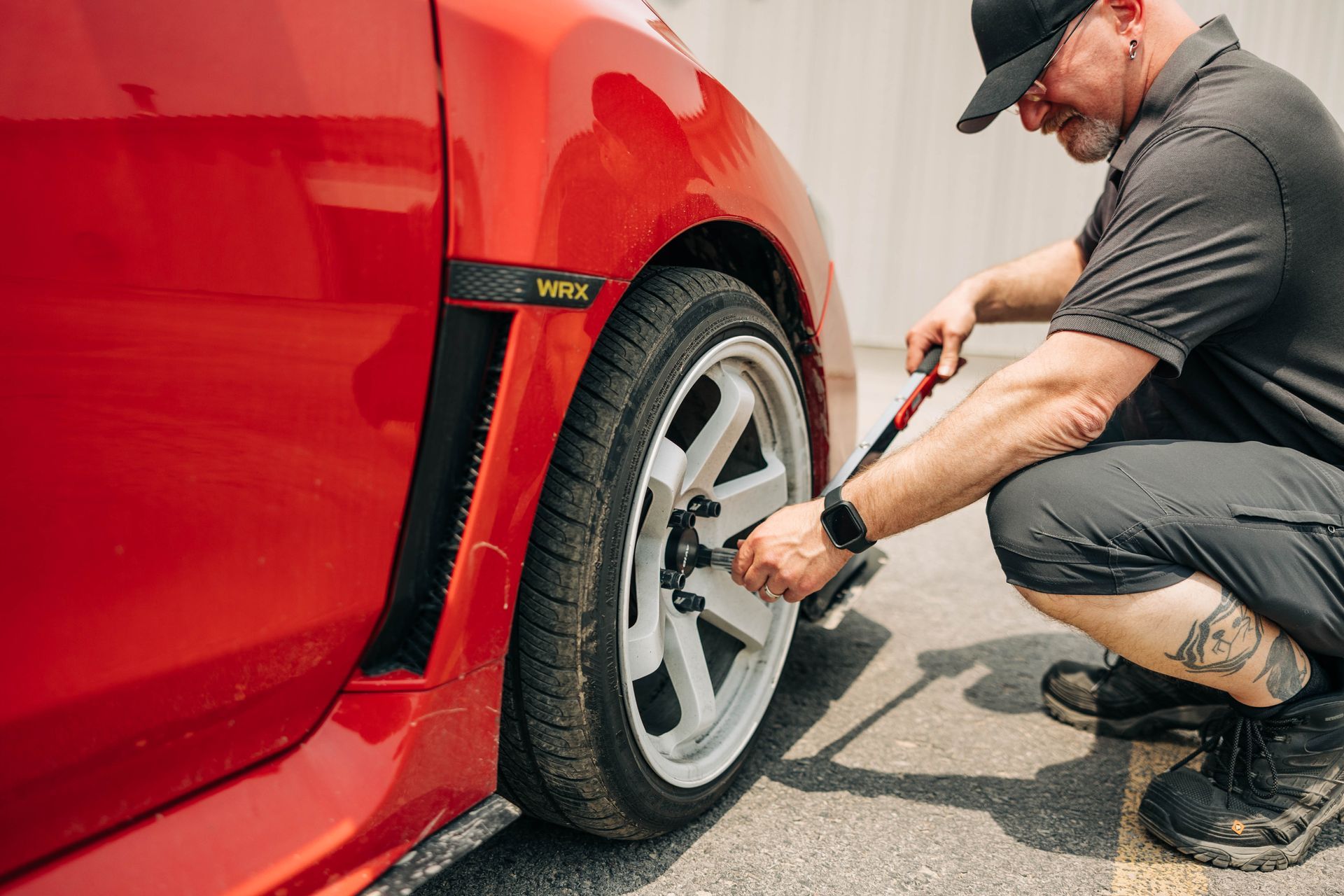 Man kneeling beside red car, using a wrench to loosen lug nuts on the wheel. | Empower Automotive