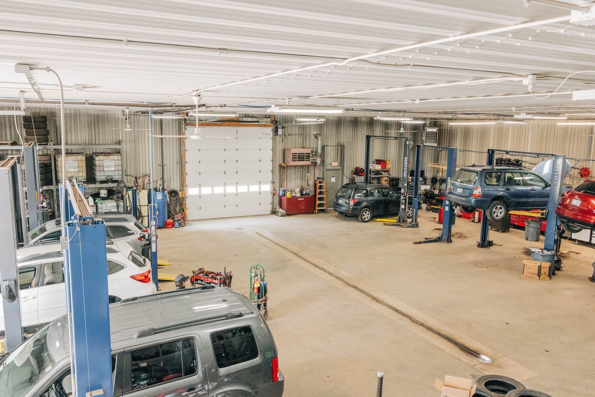 Auto repair shop interior with vehicles on lifts, open garage door, and tools. | Empower Automotive