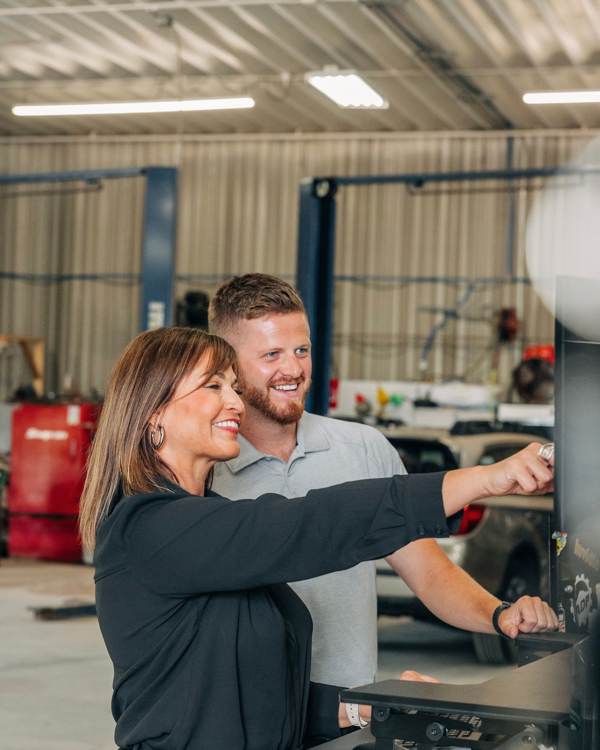 Woman and man in auto shop, woman points at a machine, both smile. | Empower Automotive