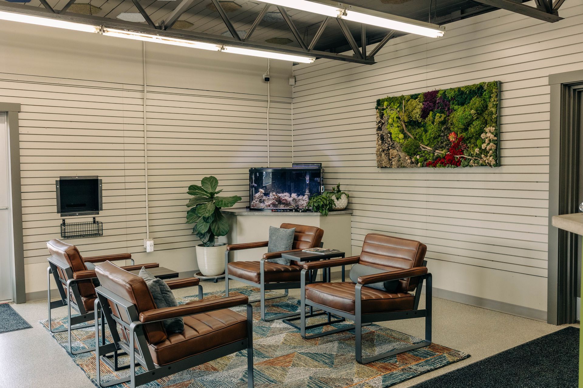 Lounge area with brown leather chairs, a TV, and a plant. A moss art piece hangs on the wall. | Empower Automotive