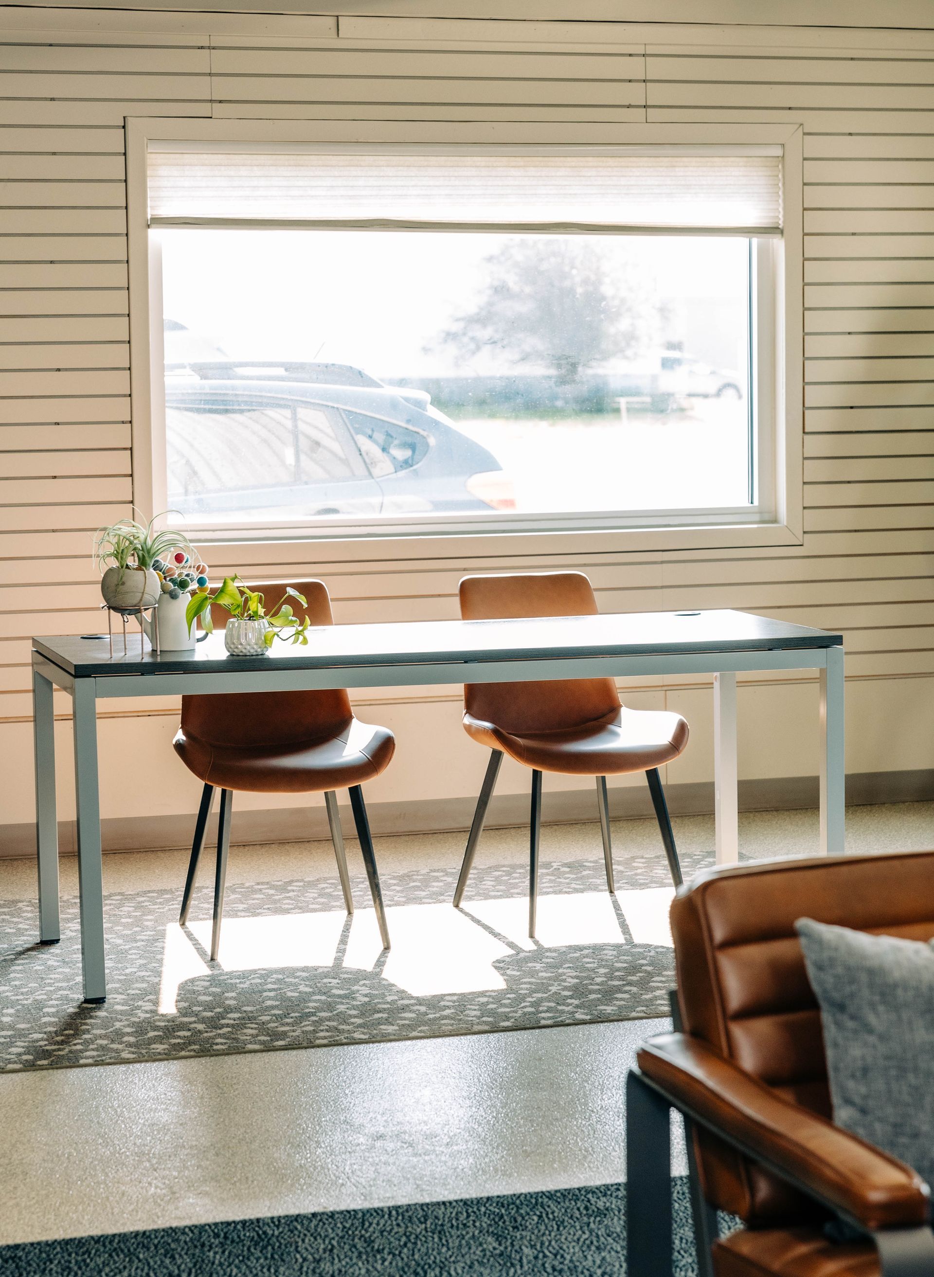 A room with a desk, two chairs, and a window overlooking a sunny view. The wall is painted white. | Empower Automotive