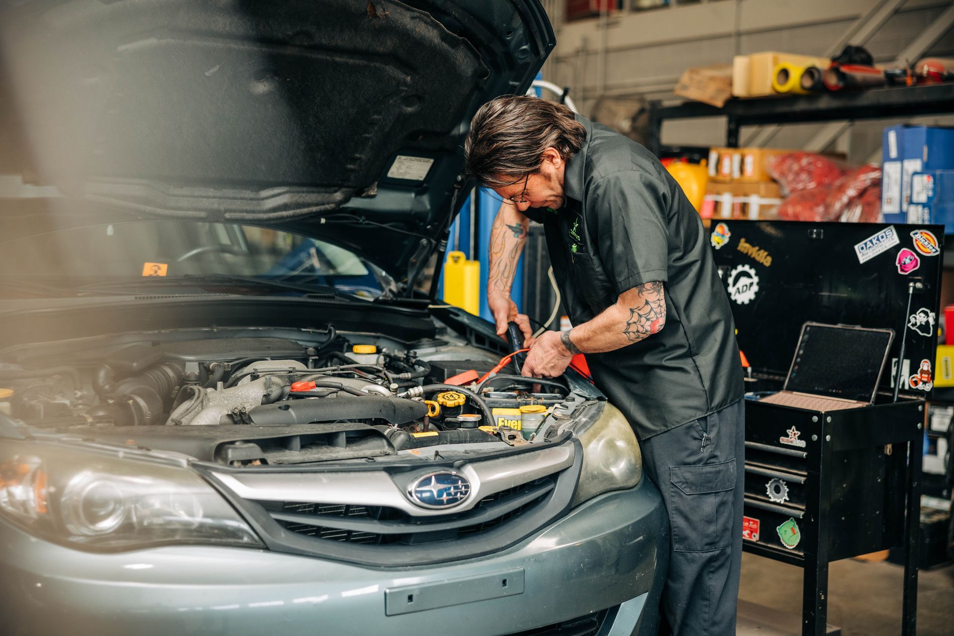 Mechanic working on a car engine in a garage. He is using tools on a gray Subaru. | Empower Automotive