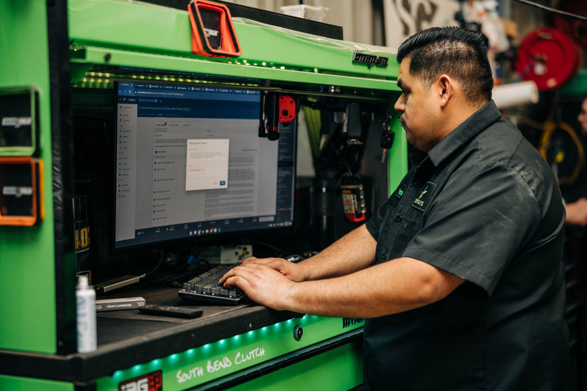 Mechanic in a green workshop, typing on a computer. | Empower Automotive