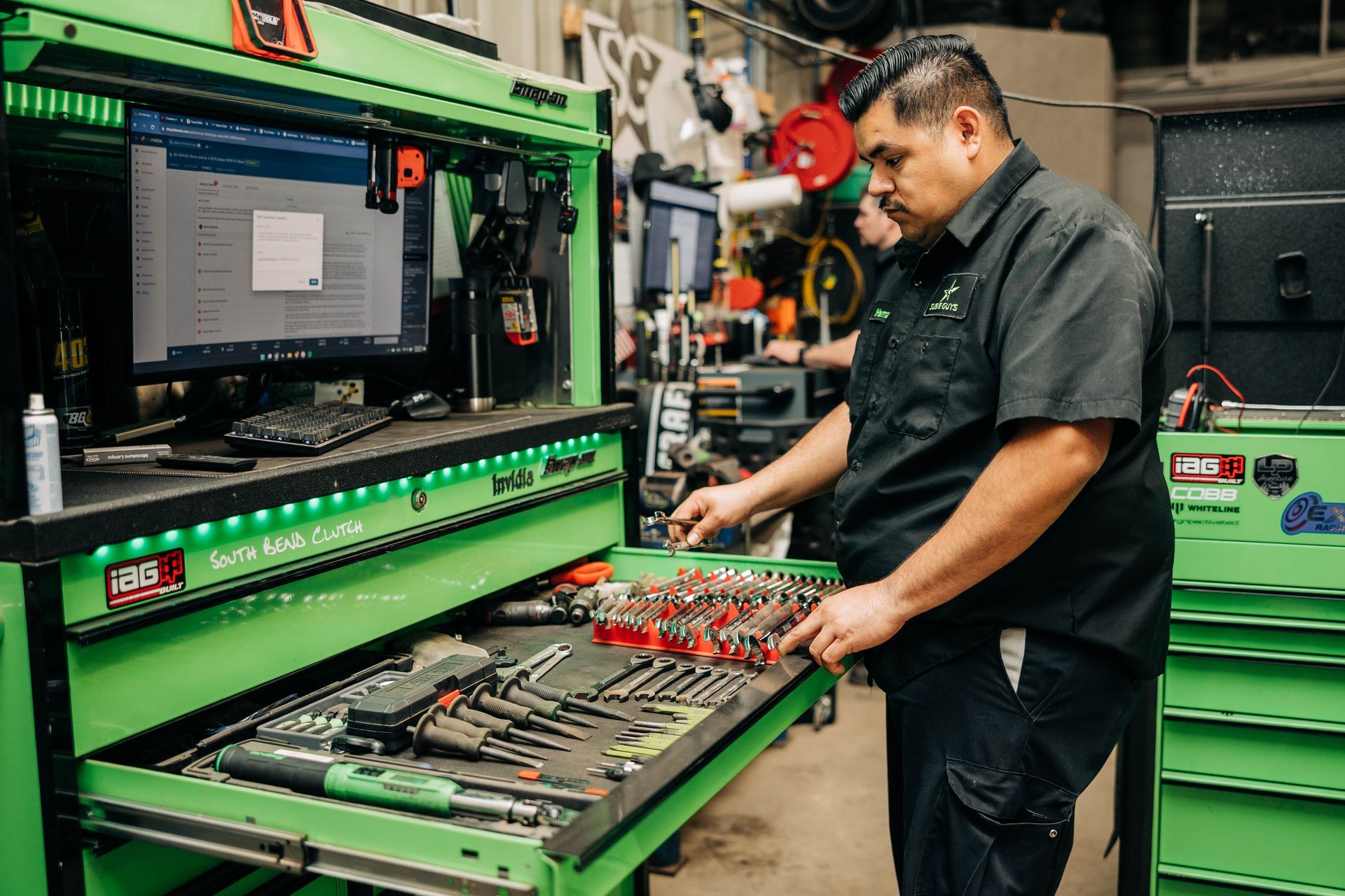 Mechanic at a green workstation in a garage, looking at tools. Computer visible. | Empower Automotive