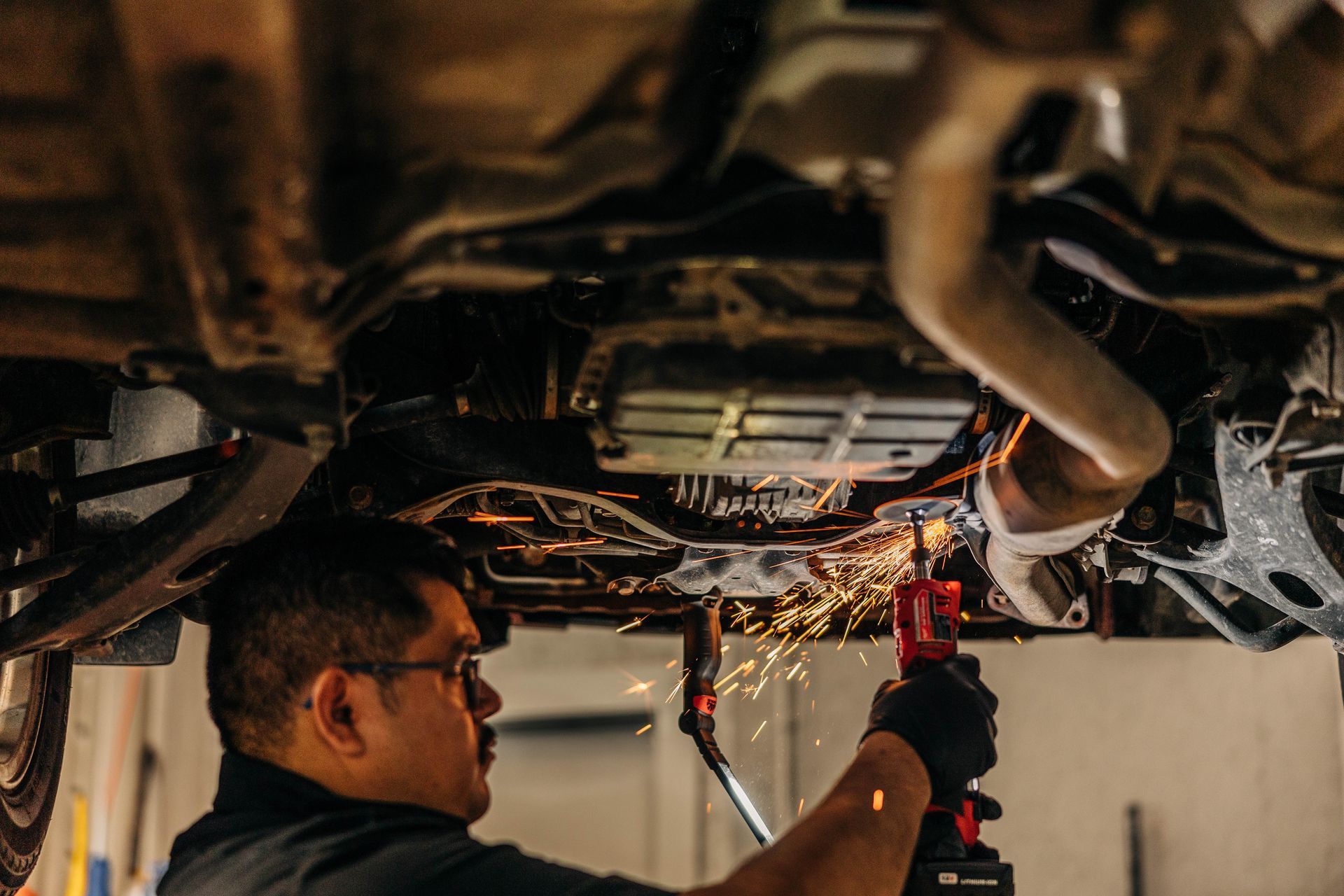 Mechanic using a grinder under a car, creating sparks. | Empower Automotive
