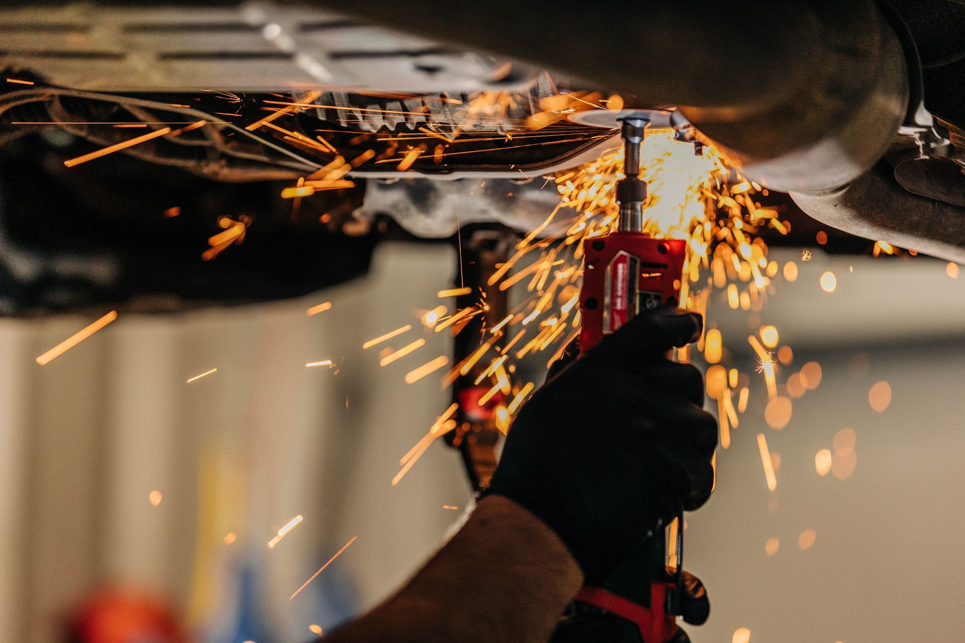 Person in black gloves using a tool to cut metal, creating sparks under a vehicle. | Empower Automotive