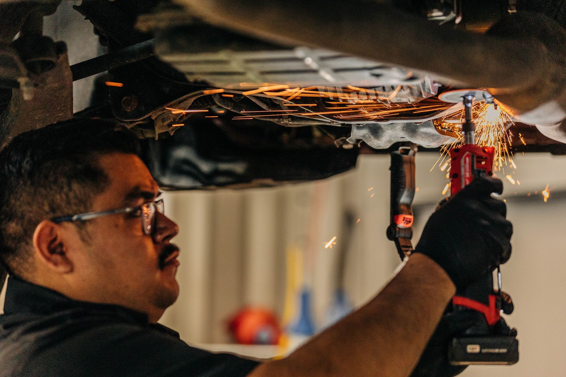 Mechanic welding under a vehicle, sparks flying. Wearing gloves and glasses, in a garage. | Empower Automotive