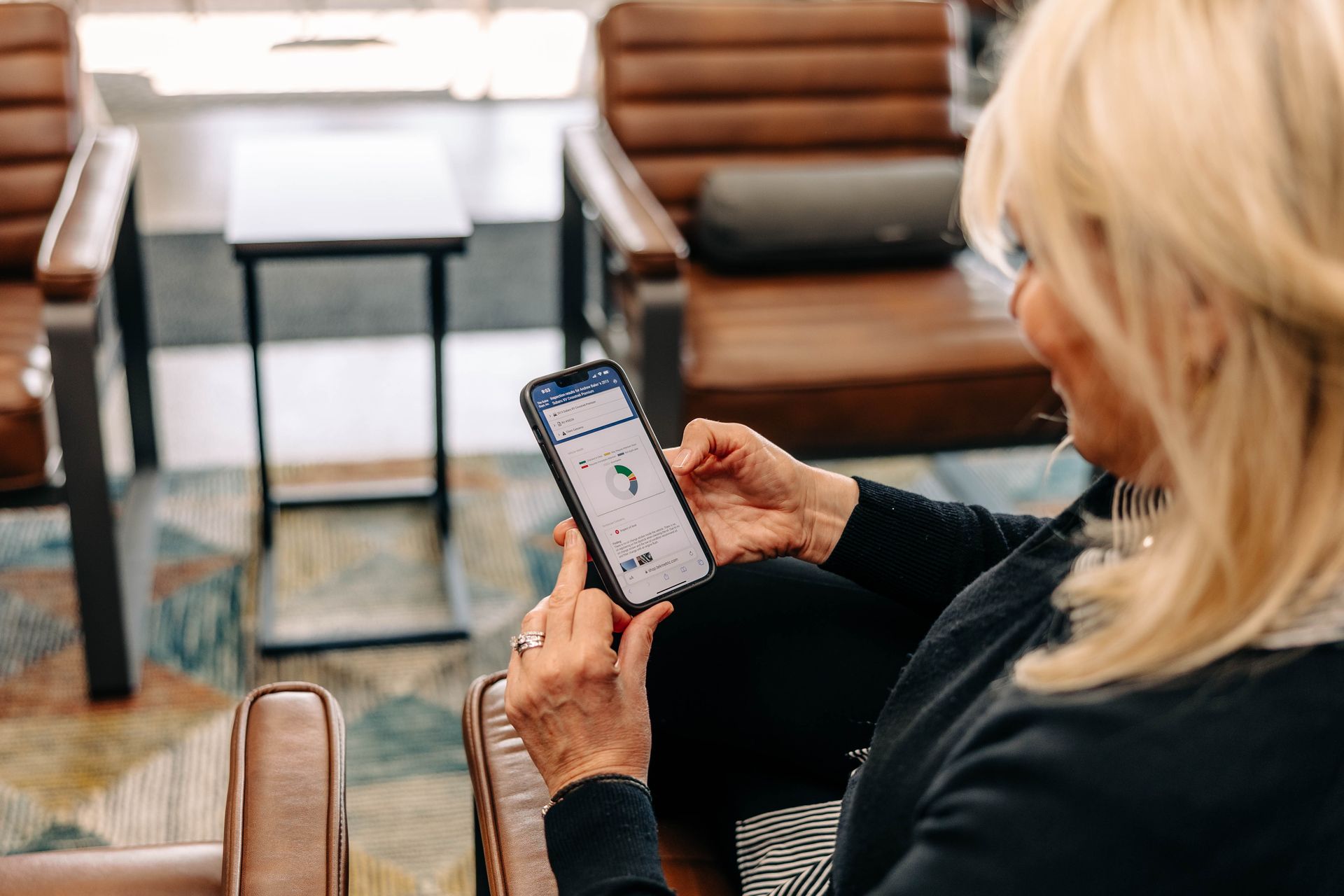 Woman with blonde hair using a smartphone, seated in a leather chair, indoors. | Empower Automotive
