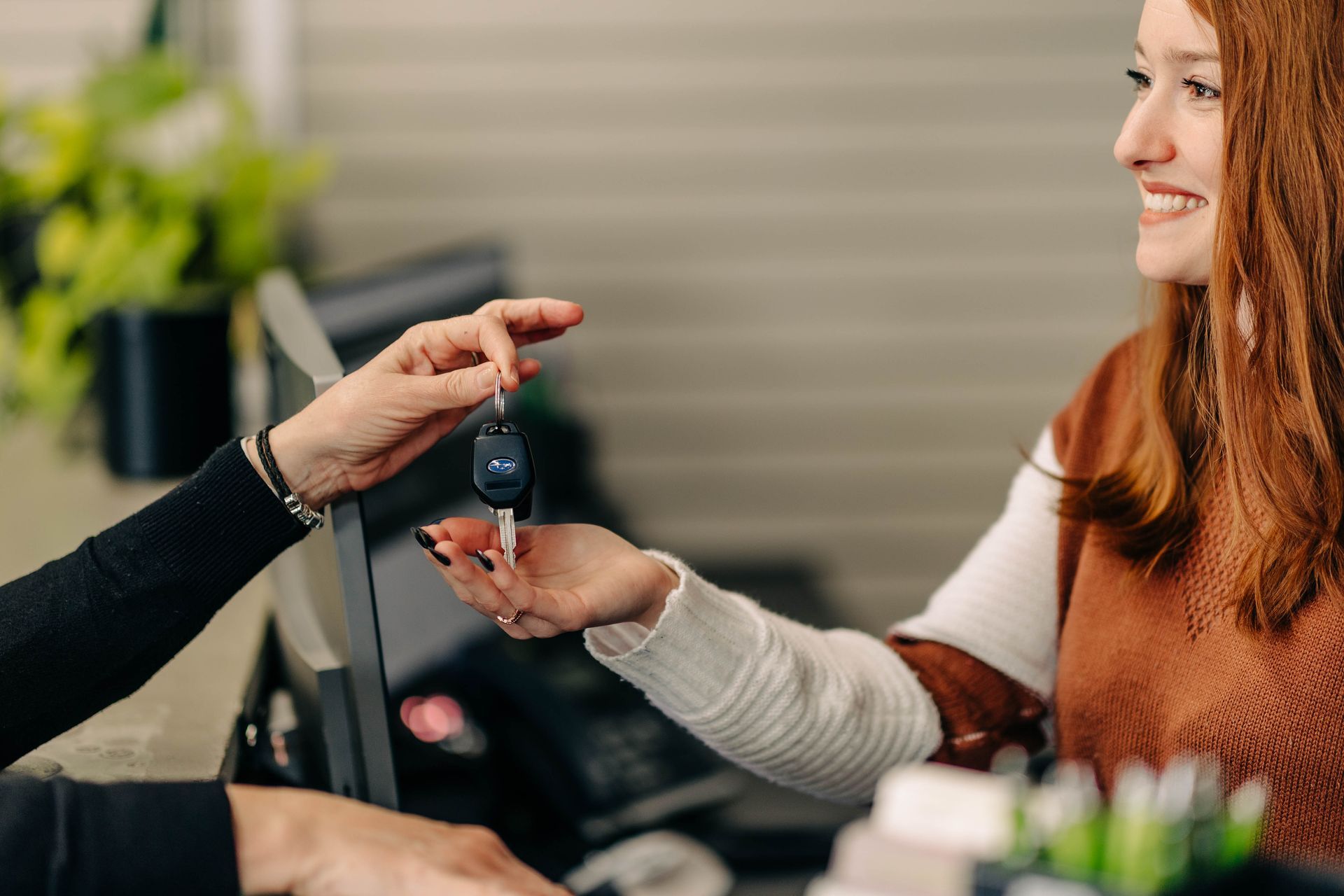 A woman receives car keys from a person behind a counter; interior setting with plants. | Empower Automotive