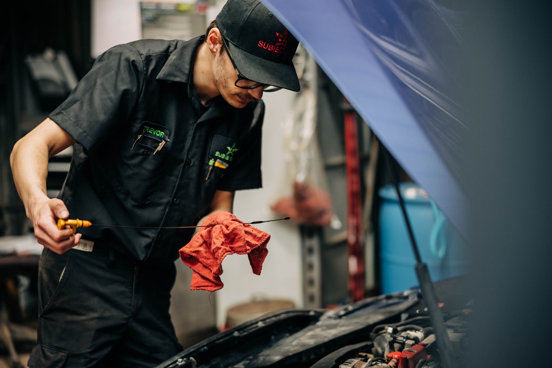 Mechanic checking oil level in a car engine, wearing a black cap and uniform, in a garage. | Empower Automotive