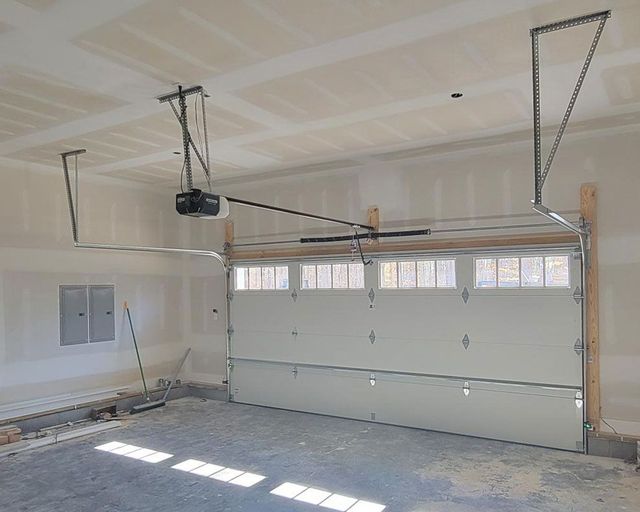 A garage with a garage door open and a garage door opener hanging from the ceiling.