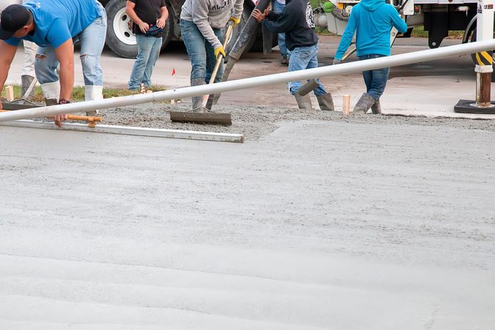 Workers pouring and leveling concrete on a paved surface.