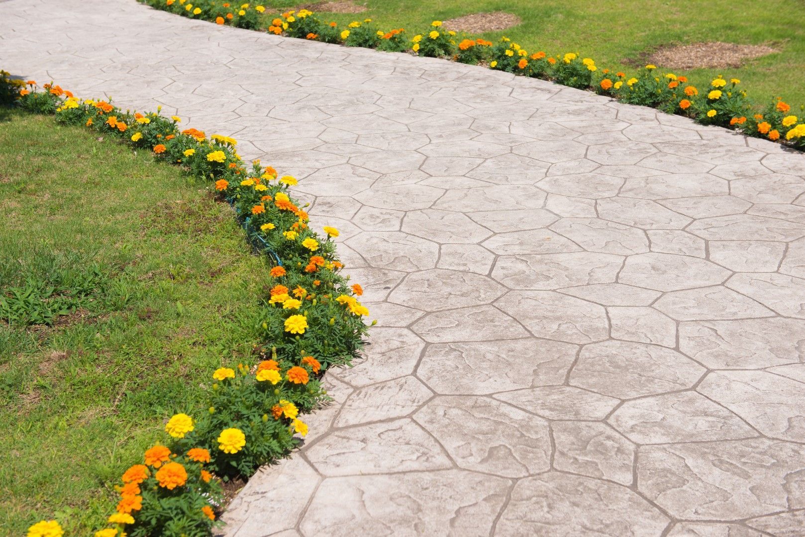 Winding stone path lined with orange and yellow flowers, curving through green grass.