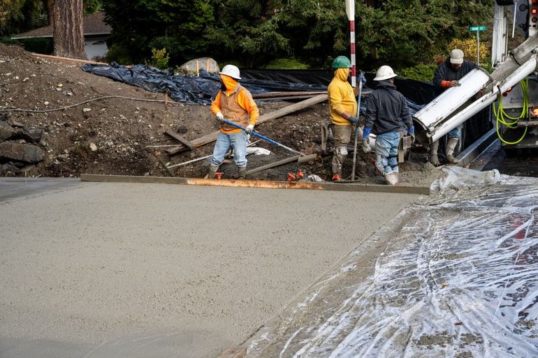 Construction workers pouring concrete on a road. Workers in orange and yellow vests, hard hats, and a concrete truck.