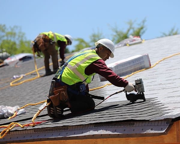 A man is working on a roof while another man looks on.