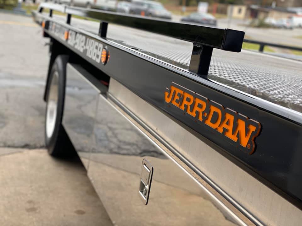A jerry dan tow truck is parked on the side of the road