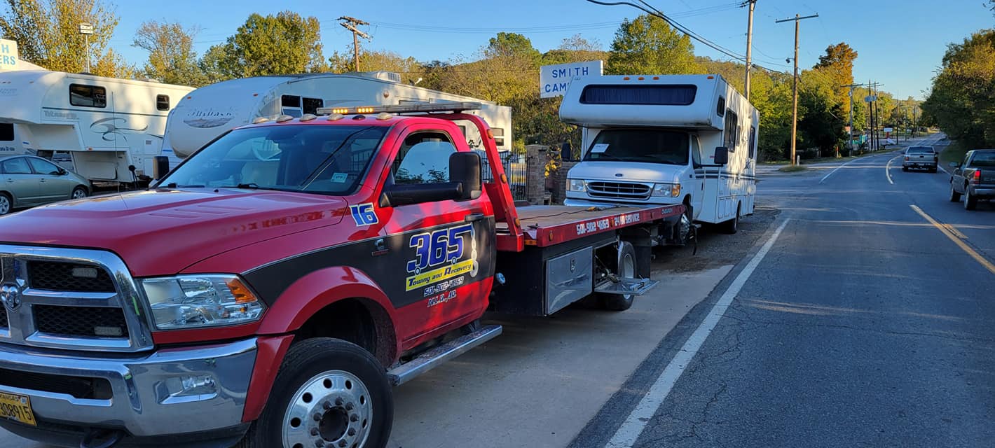 A red tow truck is towing a camper down a street.