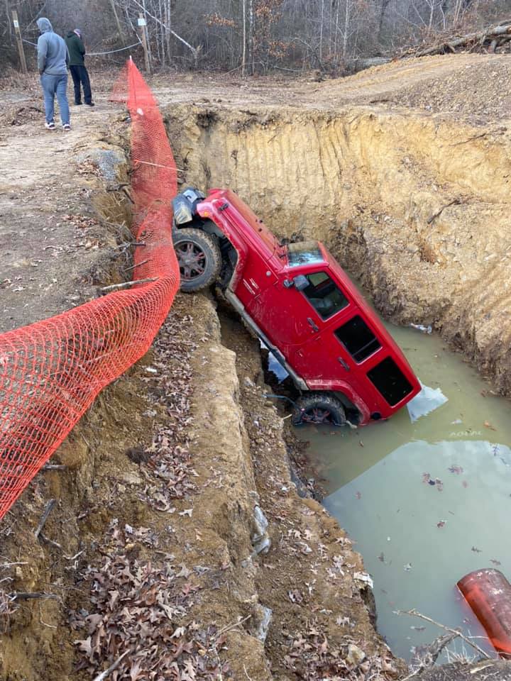 A red jeep is stuck in a hole in the ground.