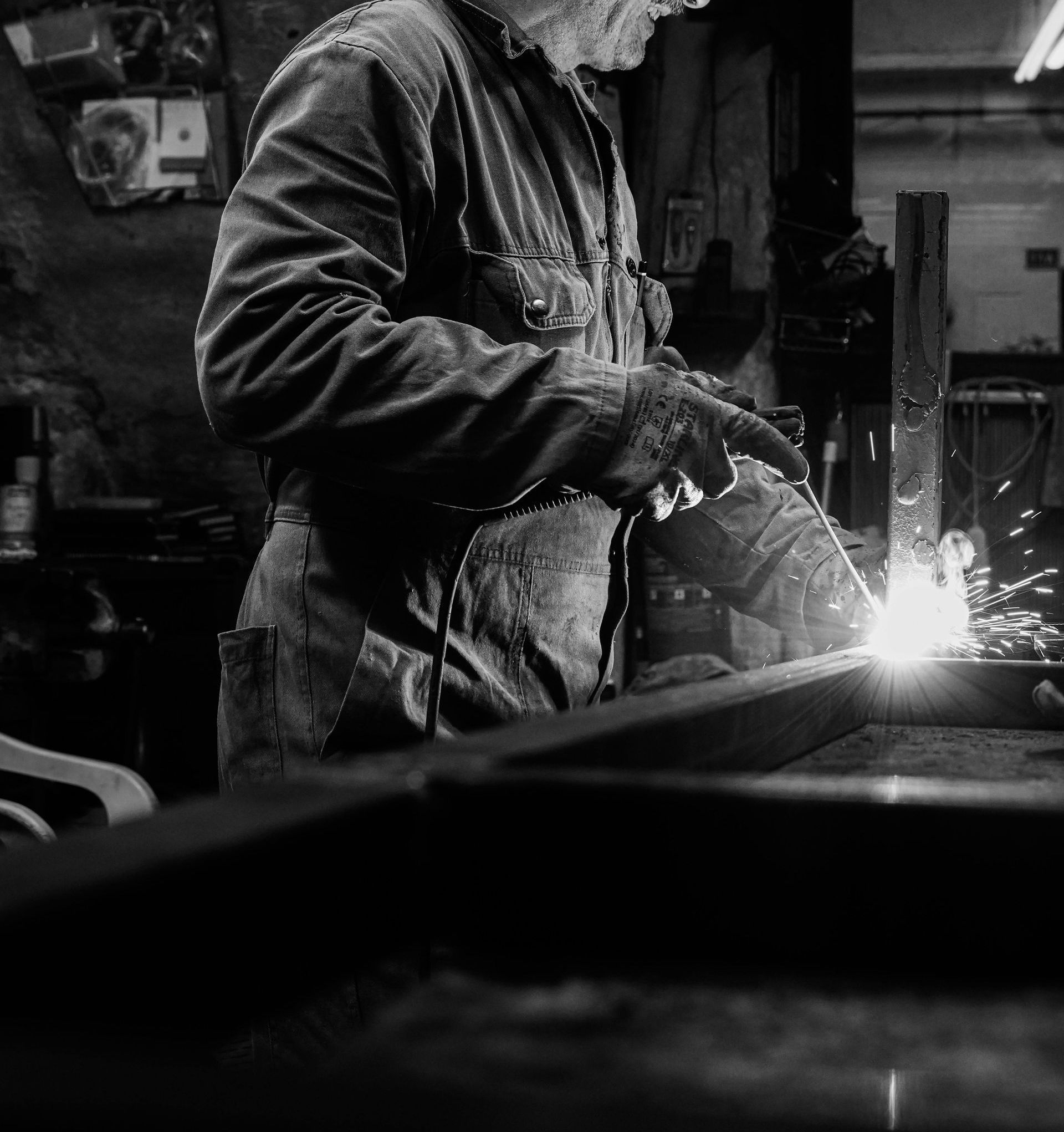 A man is welding a piece of metal in a black and white photo.