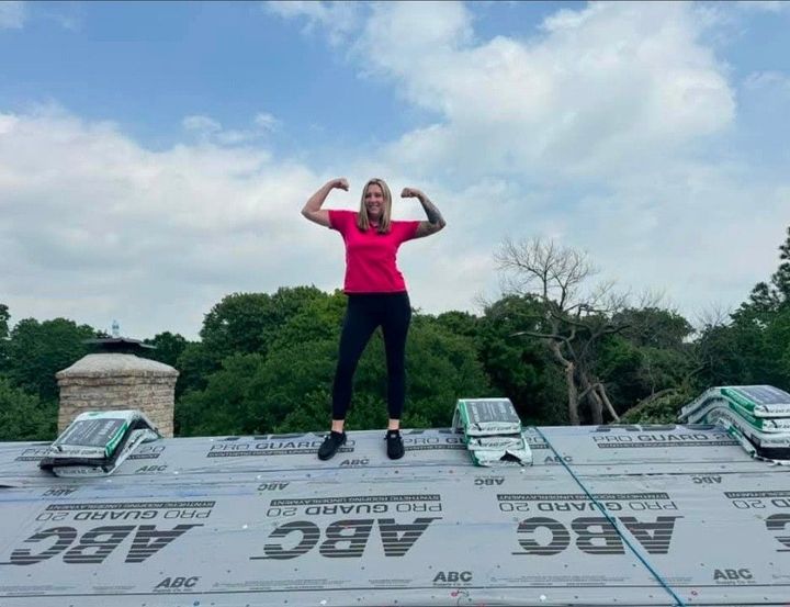 Person in a pink shirt flexing on a rooftop under a cloudy sky.