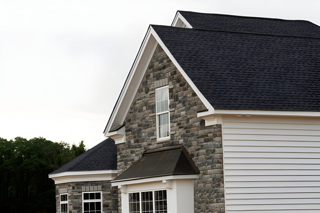 A large stone house with a black roof and white siding