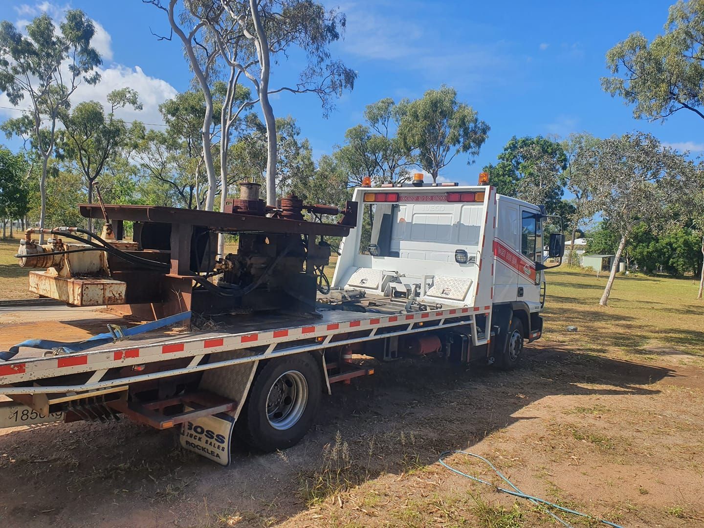 A white tow truck with a flatbed is parked in a field.