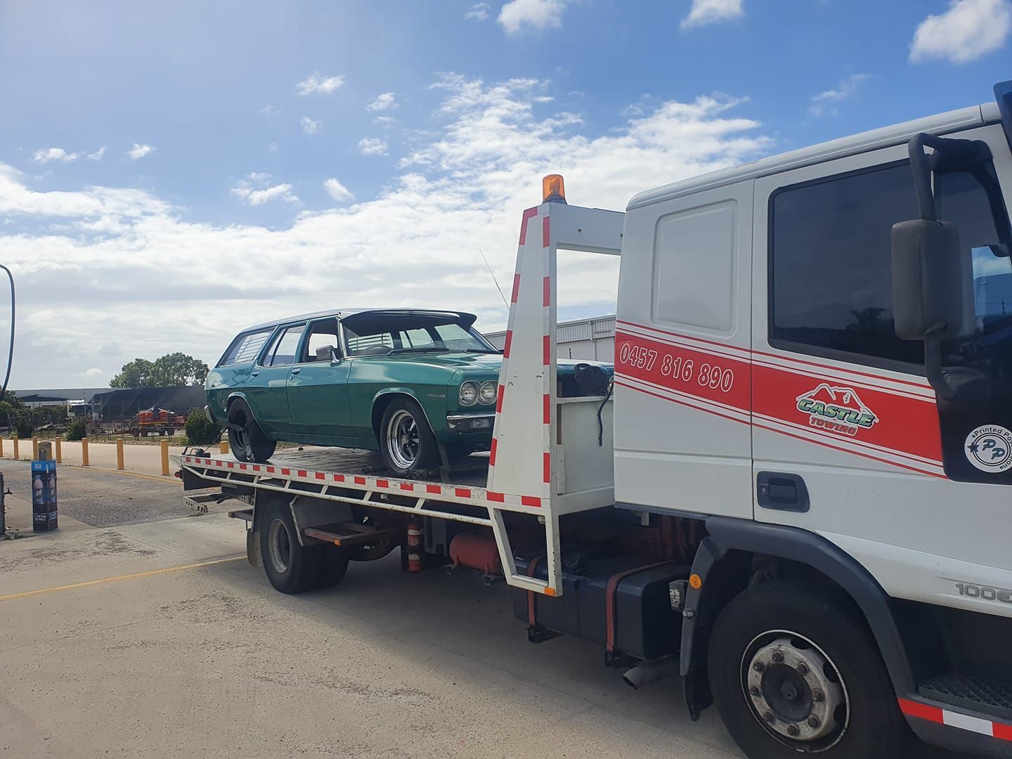 A tow truck is carrying a green car on the back of it.