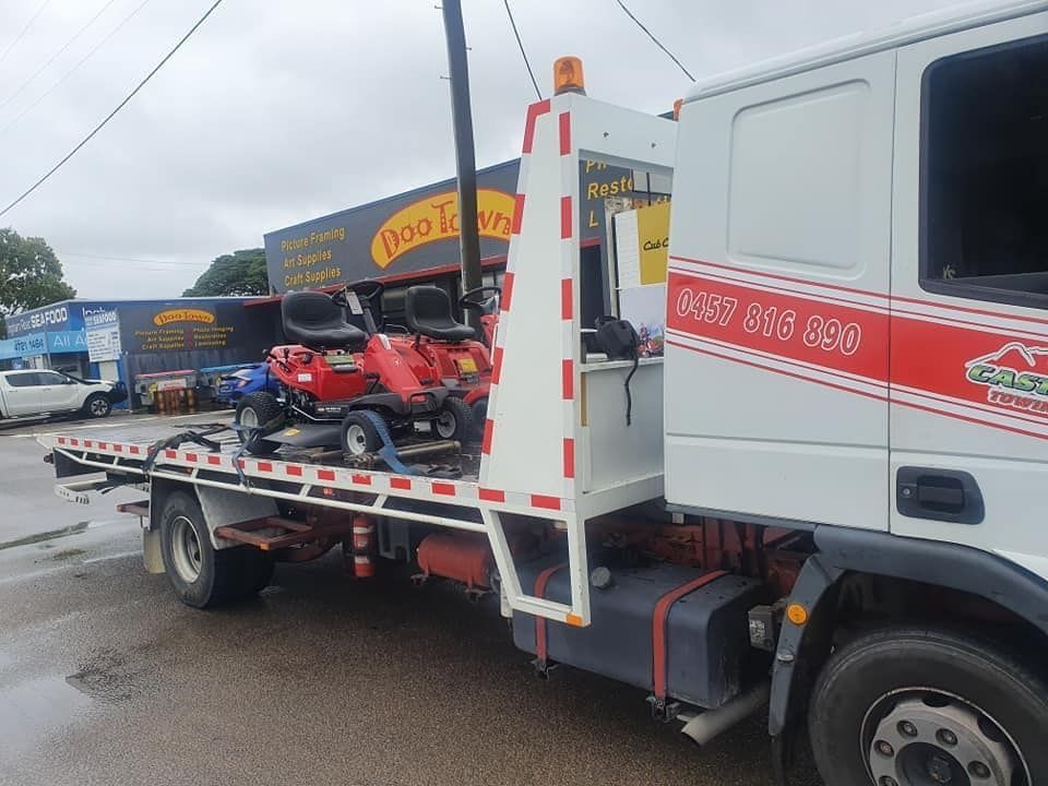 A tow truck is carrying a lawn mower on the back of it.