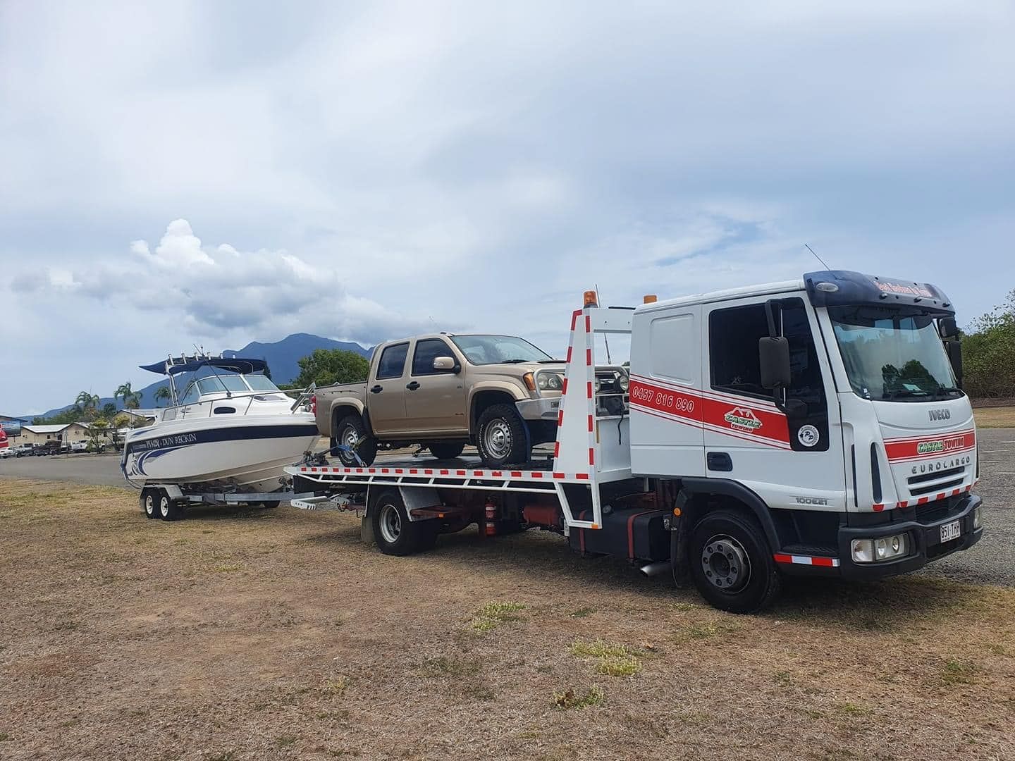 A tow truck is towing a boat and a truck.