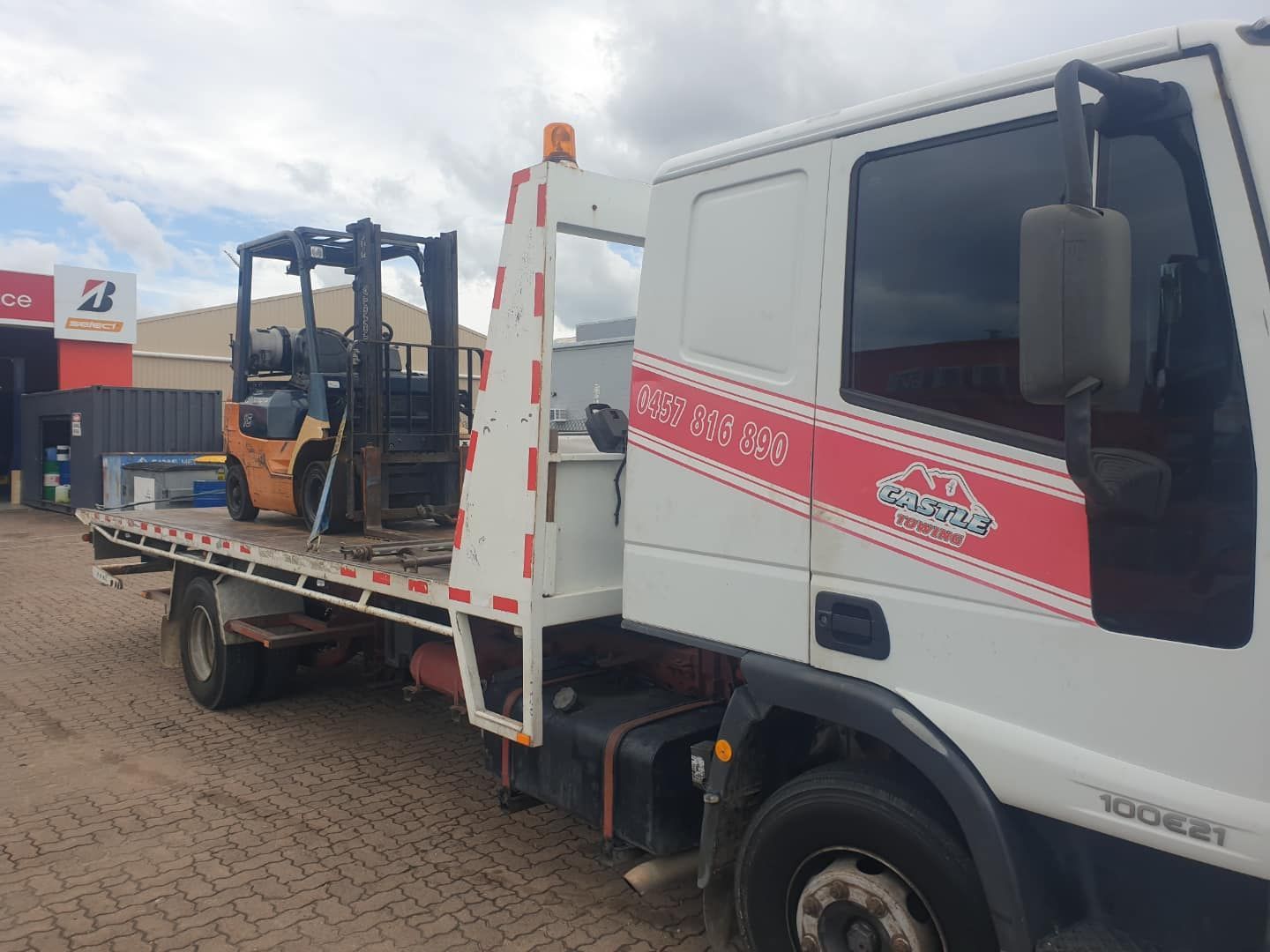 A forklift is sitting on the back of a tow truck.